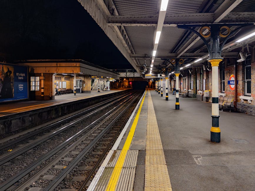 Nighttime view of Crayford Station platform, with empty railway tracks running parallel to the edge of the platform. The platform surface is paved with concrete and features tactile paving strips and 
